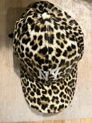 Leopard keps  - Säljer en cool keps med leopard print och bokstäverna NY på. Osäker på vilken material den är gjord av men är vattentät. Måtten kan man se på sista bilden! 