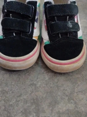 Färgglada sneakers för barn, strl 20 - Säljer ett par Vans sneakers för småbarn i storlek 20. Skorna har svart mocka framtill, vita sidor med färgglada detaljer och kardborreband för enkel påtagning. Klassisk gummisula med rutmönster och rosa rand runt sulan.