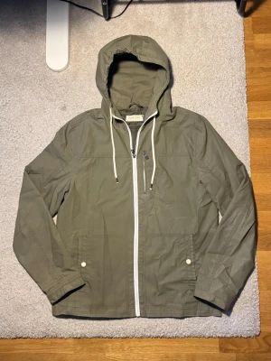 Pier One grön jacka med huva - Grön jacka från Pier One i fint skick. Lätt och bekväm med huva, dragkedja och praktiska fickor – perfekt för vår/höst eller mildare dagar. 🌿 Använd men väl omhändertagen.  Väldigt sällsynt och eftertraktad modell som inte längre säljs i butik.  📦 Skickas inom 24 timmar 🚭🐾 Från rök- och djurfritt hem 💰 Snabb affär = bättre pris, hör av dig!