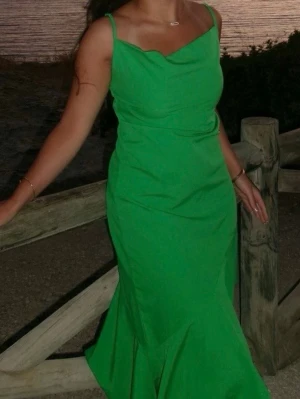 Grön asymmetrisk klänning med volang - Snygg grön klänning med smala axelband och asymmetrisk nederdel med volang. Klänningen har en figurnära passform.