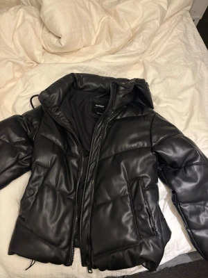 Svart pufferjacka - Säljer en svart pufferjacka från Pull&Bear i storlek S. Materialet är syntet med skinnkänsla och jackan har två fickor med knappstängning. Perfekt för kalla dagar när du vill vara både varm och snygg. Knappt använd💗
