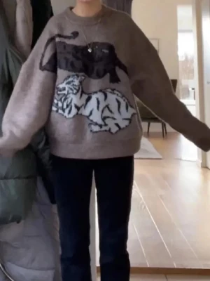 Brun oversized stickad tröja med tigrar - Säljer en brun oversized stickad tröja med stora motiv av två tigrar i svart och vitt framtill. Tröjan har rund halsringning och långa ärmar med en riktigt chill och avslappnad vibe. Perfekt för dig som gillar statement-plagg och djurmönster.