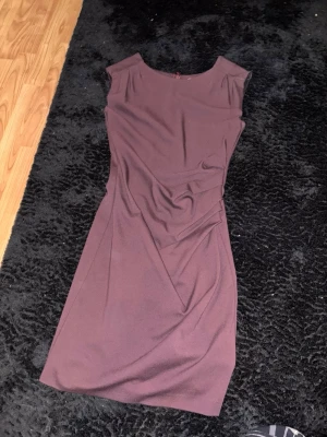 Vinröd / mörklila klänning från Tiger of Sweden - Säljer en stilren vinröd/mörklila klänning från Tiger of Sweden, modell MEKA. Klänningen är figurnära med snygga draperingar i midjan och har en klassisk rund halsringning. Perfekt för dig som gillar en elegant look.