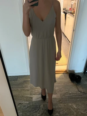 Finn ljusgrå/beige långklänning - Säljer en stilren ljusgrå/beige långklänning med smala axelband och v-ringning både fram och bak. Midjan är väldigt stretchig så den passar en xs, s och m, endast använd till ett tillfälle så sen är som ny. 