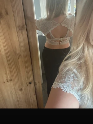 Vit spetsblus - Säljer en vacker vit spetsblus med korta ärmar och fina spetsdetaljer. Blusen har en v-ringad design och en dekorativ kant nedtill. Perfekt för en elegant look.