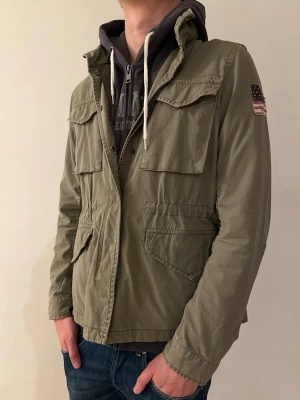 Ralph Lauren Fieldjacket Olivgrön  - Nu säljer vi denna olivgröna fältjackan med fyra stora fickor framtill och en amerikansk flaggpatch på ärmen från Ralph Lauren i storlek M|skick 8/10| Jackan har dragkedja och tryckknappar, luva som enkelt går att fälla ut och in. Perfekt för dig som gillar en snygg och stilren stil! Pris går att diskutera vid snabb affär och vid fler frågor är det bara att hojjta till! MVH VMresell✌️