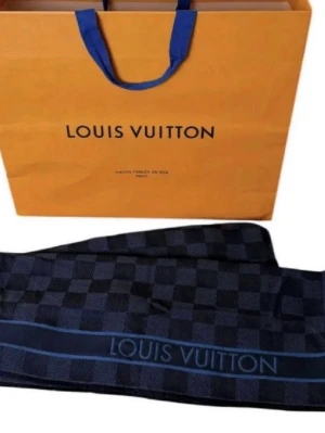 Louis Vuitton halsduk - Exklusiv halsduk från Louis Vuitton i mörkblå och svart rutig design med röda och vita detaljer på kanten. Halsduken har fransad avslutning och Louis Vuitton-logga invävd längs sidan. Perfekt accessoar för dig som vill sticka ut med lyxig stil.