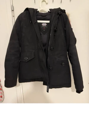 Äkta Canada Goose montebello parkajacka XS - Svart montebello parkajacka från Canada Goose med riktig avtagbar päls på huvan, dragkedja och knappar framtill samt flera fickor. Jackan har lång ärm och klassisk patch på axeln. Perfekt för kalla dagar och har en snygg, tidlös look. Har slitage på armarna och en liten fläck på framsidan på ena fickan. ✨
