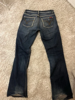 Mörkblå bootcut jeans från Levis - Säljer ett par mörkblå Levis jeans med bootcut passform och snygga slitningar framtill. Super coola detaljer på bakfickorna också! 