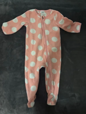 Rosa Fleeceoverall  - Mysig rosa fleecepyjamas från bpc med stora vita prickar och dragkedja framtill. Perfekt för kalla nätter och supermjuk mot huden. Heltäckande modell med långa ärmar och ben.