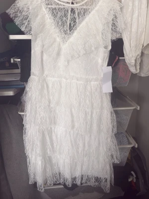 Vit spetsklänning från Bubblerolm - Supersöt vit spetsklänning med v-ringning och volangdetaljer. Klänningen har kort ärm, omlottkänsla upptill och flera lager spets i kjolen för extra fluffig look. Perfekt för sommarens alla tillfällen och har knytning i nacken. Aldrig använd!