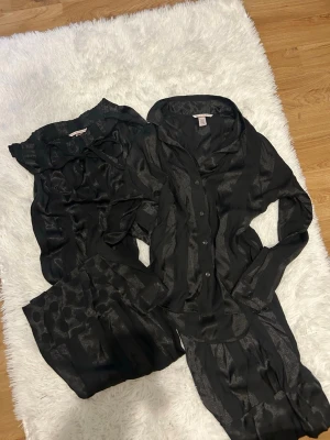 Svart randig väst från Victoria's Secret - Säljer en svart väst från Victoria's Secret i glansigt material. Västen har diskreta ränder och knappar framtill. Materialet känns lyxigt och har en lätt skimrande finish. Perfekt för dig som vill ha en stilren och elegant look.