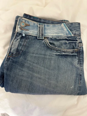 Blå bootcut jeans  - Säljer ett par blå bootcut jeans med låg midja och snygga slitningar, från Only. Jeansen har ljusare detaljer på fickor och midja samt en unik bakficka med kontrastfärg. ‼️Storlek W29 L34, men sitter som w27 L34!!!‼️Säljer då de blivit för stora men skicket är super!