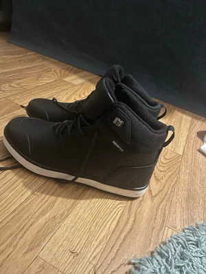Svarta sneakers från McKinley strl 41 - Helt oanvända Svarta sneakers från McKinley med hög modell och snörning. Skorna har vit sula, diskret logga och är tillverkade i syntetmaterial med textildetaljer. Perfekta för dig som vill ha en sportig och clean look. Modellen heter NELL II MID AQX.