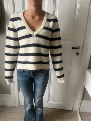 Randig stickad tröja med v-ringning - Säljer en mysig stickad tröja med breda svarta och vita ränder. Tröjan har v-ringad hals, lång ärm och ribbade muddar. Perfekt till jeans för en chill look. Passformen är normal och materialet känns mjukt och skönt.