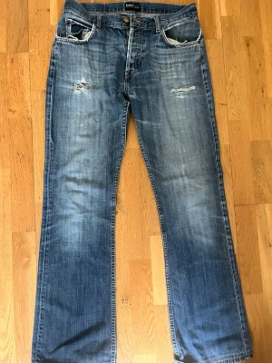 Blå Lee jeans med slitningar - Säljer ett par blå jeans från Lee i modellen ”DENVER” Jeansen har raka ben och normal passform o snygga slitningar framtill. Är i storlek W33 L36 men VÄLDIGT små i i storleken, Passar mig som brukar ha st 38, W28/29 L32!! Skriv om du vill ha måtten!!