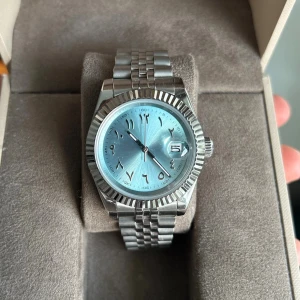 Seiko Mod klocka - Säljer nu en riktigt snygg seiko klocka som är modifierad, Det som är nytt är självaste urtavlan som är en mer stilig is/ himmelsk blå färg med arabiska siffror och utan seiko text.  Klockan är en automatisk klocka med mättet 39 mm. Märke: Seiko. Urverk: NH36A. Glas: Safir. Armband: Rostfritt stål.  Klockan är i mycket bra skick och allt fungerar som det ska. Klockboxen till höger medföljer! Skriv till mig om ni har några funderingar, jag är även öppen för bud!