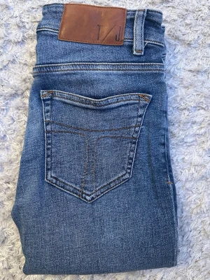 Tiger of Sweden skinny jeans blå 27/30 - Snygga blå jeans från Tiger of Sweden med klassisk femficksdesign och läderpatch bak. Jeansen har en tight passform och är tillverkade i stretchigt denim för extra komfort. Perfekta för dig som gillar en smal siluett och stilren look.