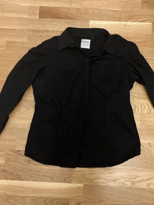 Svart skjorta från Esprit - Klassisk svart skjorta från Esprit med lång ärm och knappar framtill. Skjortan har en tidlös design med krage och är tillverkad i mjukt bomullstyg som känns skönt mot huden. Perfekt till jeans eller kjol för en clean look.