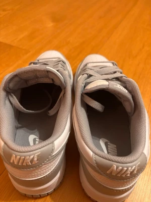 Nike Dunk Low vit/grå sneakers - Nike Dunk Low sneakers i vitt och ljusgrått skinn med klassisk swoosh på sidan.Tidlös och clean look som passar till det mesta. Bekväm innersula och slitstark yttersula. Har slängt både lådan och kvittot då skorna passade under vintern men hann tyvärr bli för små inför sommaren. Skorna är också helt oanvända. 