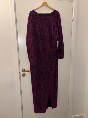 Glittrig långklänning från SHEIN Curve - Säljer en svart och lila glittrig långklänning från SHEIN Curve. Klänningen har lång ärm, ett coolt randigt mönster och en slits framtill. Materialet är syntetiskt och skimrar snyggt i ljuset. Perfekt för dig som vill sticka ut!