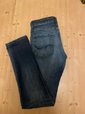 Slim Glenn blå jeans 28/32 - Mörkblå jeans från Slim Glenn i storlek 28/32. Klassisk femficksmodell med snygga slitningar och kontrastsömmar. Jeansen har slim fit passform och raka ben, perfekta till sneakers eller boots. Materialet är mjukt och följsamt jeans-tyg.