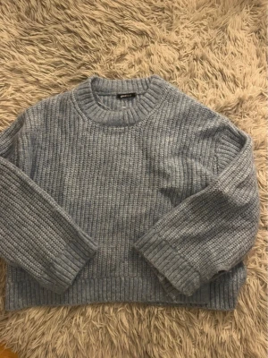 Blå stickad tröja från Gina Tricot - Mysig blå stickad tröja från Gina Tricot med grov ribbstickning. Tröjan har rund halsringning och långa ärmar med breda muddar. Perfekt för kyliga dagar och enkel att styla med jeans eller kjol.