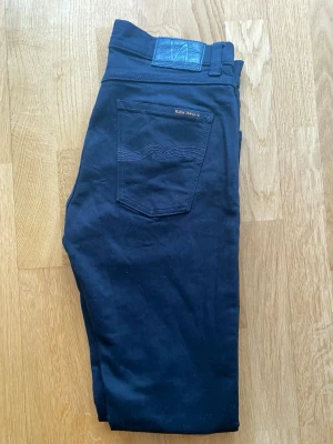 Svarta Nudie Jeans 30/32 - Säljer ett par svarta jeans från Nudie Jeans i storlek 30/32. Modellen har klassisk femficksdesign och snygga detaljer på bakfickorna. Jeansen är tillverkade i ett mjukt bomullsmaterial och har en stilren look som passar till det mesta. Priset går att diskutera så lägg bud!