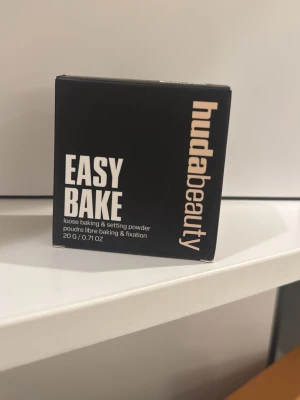 Huda Beauty Easy Bake Banana Bread - Loose baking & setting powder från Huda Beauty i nyansen Banana Bread. Kommer i en svart fyrkantig förpackning med tydlig beige etikett. Pudret är lätt och ger en matt finish, perfekt för att fixera sminket och highlighta ansiktet. Innehåller 20 g. OBS boka med PostNord! 
