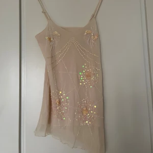 Ljusgul asymmetrisk paljettopp - Ljusgul topp med justerbara tunna axelband och asymmetrisk nederkant. Toppen har glittriga paljettdetaljer och broderade blommor. Kan mötas upp på Södermalm!