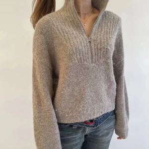 Beige stickad tröja med half zip - Mysig beige stickad tröja med ribbad detalj upptill och hög krage med half zip. Tröjan har en loose passform och långa ärmar, perfekt för lager-på-lager under kyliga dagar. 