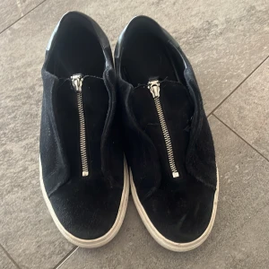 Svarta sneakers med dragkedja - Svarta sneakers med vit sula och snygg dragkedja framtill istället för klassisk snörning. Ovandelen är i mocka och detaljer i skinn, vilket ger en cool kontrast. Söm har gått upp lite ovanpå skon - se bild 3. 