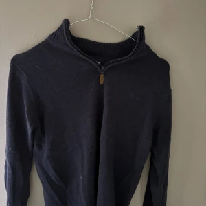 Mörkblå stickad tröja med half zip - Snygg mörkblå stickad tröja med ribbad krage och half zip-dragkedja. Perfekt för dig som gillar enkel och stilren design. Långärmad modell som passar till jeans eller chinos. Skön och mjuk känsla tack vare det stickade materialet.