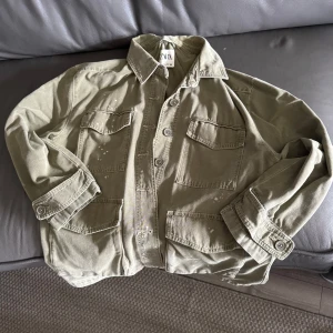 Olivgrön overshirt från Zara - Olivgrön overshirt från Zara med fyra stora fickor framtill och coola knappar. Snygga vita färgstänk ger en unik touch. Stor i storleken och använd max 4 gånger 