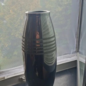 En Vas - Bilderna visar en svart, glansig vas med dekorativa horisontella ränder. Produkten är inte elektronik och har inga synliga märken, knappar eller funktioner som indikerar att det är en elektronisk enhet. Inga defekter eller slitage syns.