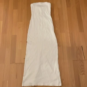 Vit axelbandslös långklänning med slits - Säljer en vit axelbandslös långklänning i ribbat material. Är 159 cm och den passar perfekt. Vid frågor och bild skriv gärna 🩷