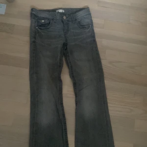 Grå jeans från Gina Tricot, storlek 158 - Säljer ett par grå jeans från Gina Tricot i storlek 158. Byxorna har klassisk femficksdesign, liten bootcut ben och snygga detaljer med knappar på bakfickorna. Perfekta för dig som gillar en enkel och stilren look.