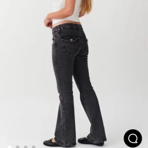 Svarta bootcut jeans med fickdetaljer - Snygga svarta jeans med bootcut passform och låg midja. Jeansen har coola bakfickor med lock och knapp, samt klassisk femficksdesign. Materialet är stretchigt jeans och färgen är tvättad svart för en trendig look. Endast använda fåtal gånger så skicket är nästan som nytt. Ordinarie pris 499 kr