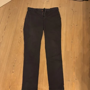 Svarta stretch-chinos från Morris - Snygga svarta chinos från Morris med stretch för extra komfort. Klassisk rak passform, bälteshällor och två bakfickor med knappar. Broderad logga ovanför ena bakfickan. Perfekta för en stilren look.