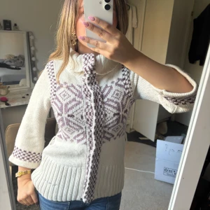 Vit kofta från Bondelid med mönster - Superfin vit kofta från Bondelid med lila mönster och stora snöflingor. Koftan har trekvartsärmar, bred krage och knappar framtill. 