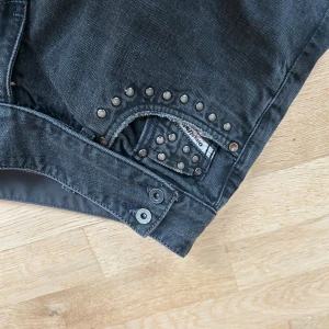 Diesel Cherone svarta jeans med nitar - Säljer ett par svarta Diesel Cherone jeans med coola nitar runt fickan och detaljerade knappar. Jeansen har en rak passform och är tillverkade i klassiskt denimtyg. Perfekta för dig som vill ha en edgy look med extra detaljer.
