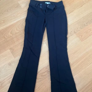 Svarta bootcut byxor från Gina Tricot - Svarta byxor från Gina Tricot i storlek 152. Byxorna har bootcut-modell med utsvängda ben och markerad söm framtill. Stängs med två knappar och dragkedja. Perfekta för dig som gillar en klassisk men trendig look.