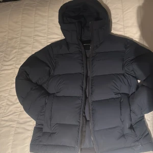  Peak Performance pufferjacka  - Kom med pris. Säljer en mörkblå pufferjacka från Peak Performance i storlek M. Köpte för 4200kr endast använt få tal gånger, slutade använda för fick en moncler i födelsedagspresent. Jackan har huva, dragkedja framtill och breda, quiltade paneler. Perfekt för kalla dagar och riktigt snygg streetstil. Materialet är mjukt och känns riktigt lyxigt.