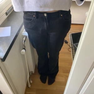 Svarta bootcut jeans - Säljer ett par svarta jeans med bootcut-modell och rå, fransad kant nertill. Jeansen har klassisk femficksdesign, knapp och dragkedja framtill samt raka ben som blir vidare nedtill. Snygg, mörk tvätt och skön passform.