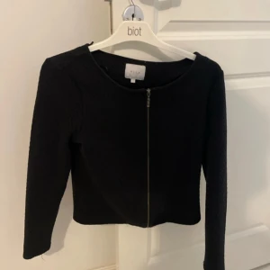 Svart kofta med dragkedja från VILA - Säljer en svart, stilren kofta från VILA med dragkedja framtill. Koftan har lång ärm och en något croppad passform. Perfekt att slänga över en topp för en clean look. Enkel och snygg design som passar till mycket.