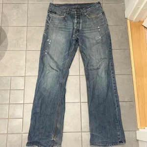 Yves Saint Laurent blå jeans bootcut - Snygga blå jeans från Yves Saint Laurent med klassisk femficksdesign och bootcut-ben. Jeansen har slitna detaljer och ljus tvätt för en avslappnad vibe. Tydlig YSL-logga på bakfickan och liten etikett fram. Perfekta för dig som gillar en tidlös men cool look.
