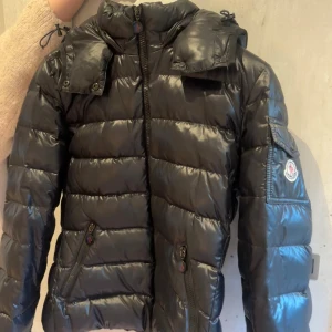 Moncler Bady jacka - Super snygg Moncler bady hooded short down jacket. Jackan har lite defekter men inget stort som märks. Vid intresse kan jag äktahets bevisa samt visa alla defekter. Skriv privat för frågor!! Nypris ca 16 200kr! Storlek 2 som motsvarar ca 38.
