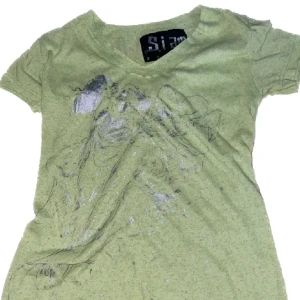Grön t-shirt med konstnärligt tryck - Cool grön t-shirt från Siam med v-ringning och ett konstnärligt tryck framtill. T-shirten har korta ärmar och är tillverkad i mjuk bomull, perfekt för en avslappnad streetstyle-look.#y2k#baddie