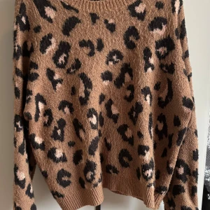 Leopardmönstrad stickad tröja Bershka - Säljer en brun stickad tröja från Bershka med leopardmönster i svart och ljusrosa. Tröjan har rund halsringning, ribbade muddar och lång ärm. Perfekt för dig som vill sticka ut med en trendig och mysig look.