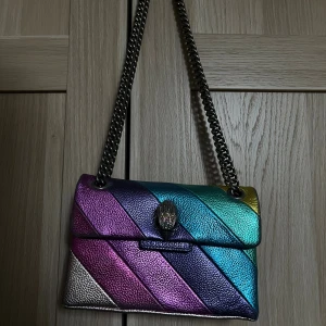 Regnbågsfärgad axelväska Kurt Geiger - Säljer en färgstark axelväska från Kurt Geiger, modell The Kensington. Väskan har regnbågsfärgade diagonala ränder i metallic och en kedjerem i mörk metall. Använd men inte yttre större skador!  Nypris är 3050 kr💖